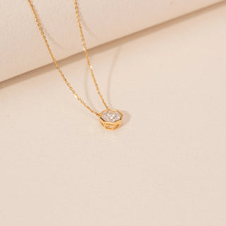 Angled view of a 14KT yellow gold necklace featuring a round-cut diamond pendant, set against a beige background.