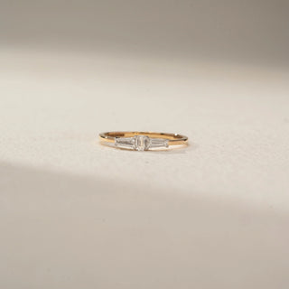 Front view of a tapered baguette diamond ring in 14 KT Yellow Gold, featuring a central emerald-cut lab-grown diamond flanked by tapered baguette side diamonds, displayed against a beige backdrop.
