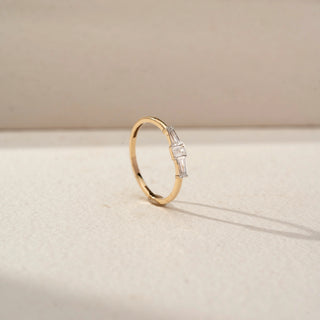 Angled view of a tapered baguette diamond ring in 14 KT Yellow Gold, featuring a central emerald-cut lab-grown diamond flanked by tapered baguette side diamonds, displayed against a beige backdrop.