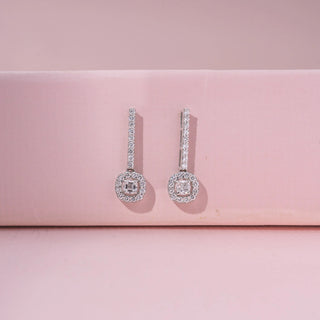 Front view of 14KT white gold earrings featuring round-cut diamonds in a circular design, set against a pink background.
