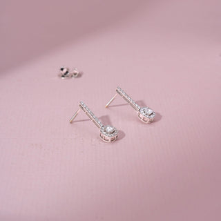Side view of 14KT white gold earrings featuring round-cut diamonds in a circular design, set against a pink background.