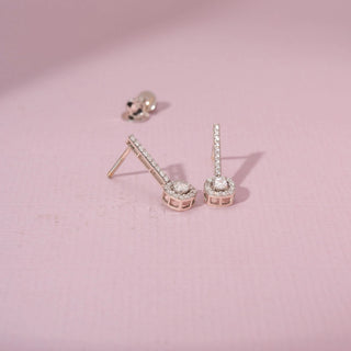 Angled view of 14KT white gold earrings featuring round-cut diamonds in a circular design, set against a pink background.