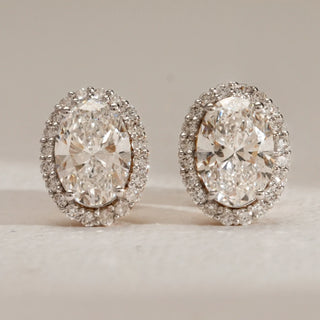 Front view of oval-cut lab-grown diamond halo stud earrings in 18KT Yellow Gold, featuring EF-VVS diamonds surrounded by a brilliant halo, displayed on a neutral surface.