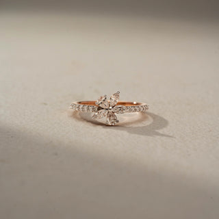 Front view of a floral diamond ring in 14 KT Rose Gold, featuring marquise-cut lab-grown diamonds arranged in a delicate flower motif atop a pavé-set diamond band, displayed against a beige backdrop.