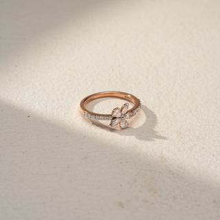 Top view of a floral diamond ring in 14 KT Rose Gold, featuring marquise-cut lab-grown diamonds arranged in a delicate flower motif atop a pavé-set diamond band, displayed against a beige backdrop.