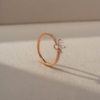 Angled view of a floral diamond ring in 14 KT Rose Gold, featuring marquise-cut lab-grown diamonds arranged in a delicate flower motif atop a pavé-set diamond band, displayed against a beige backdrop.