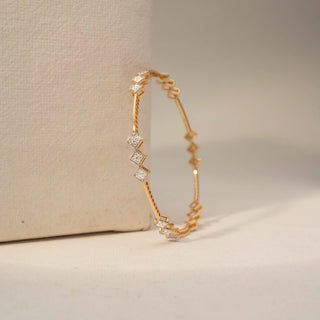 Angle view of a diamond bracelet in 18 KT Yellow Gold, featuring geometric diamond-set square motifs linked by sleek gold bars, displayed against a soft beige backdrop.