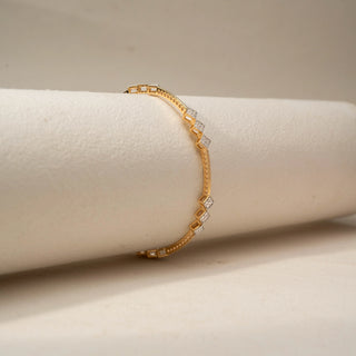 Side view of a diamond bracelet in 18 KT Yellow Gold, featuring geometric diamond-set square motifs linked by sleek gold bars, displayed against a soft beige backdrop.