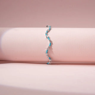 Front view of a turquoise enamel bracelet in 14KT White Gold, featuring alternating diamond clusters and curved links against a pink backdrop.