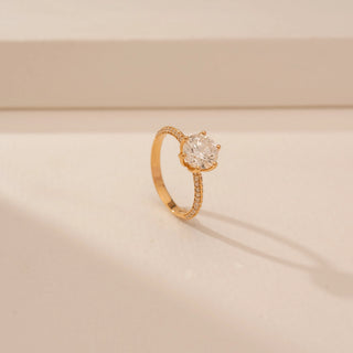 Angled view of a 14KT Yellow Gold diamond ring with a round centre diamond, six-prong setting and diamond-set shoulders.