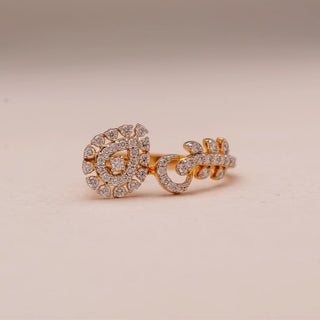Front view of Reia’s 14 KT Yellow Gold Artisan Spiral Ring. The centred pear-shaped motif and leaf-like bypass band, pavé-set with diamonds, are showcased against a soft pink surface.