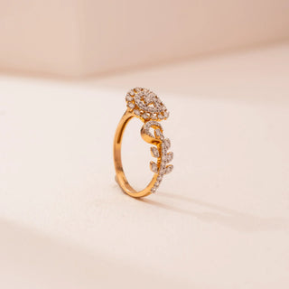 Side view of Reia’s 14 KT Yellow Gold Artisan Spiral Ring. The intricate, diamond-encrusted pear motif and leaf-like bypass band are shown on a gold band against a soft pink surface.