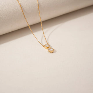 Top view of a two-stone diamond pendant in 14KT Yellow Gold, featuring round and oval bezel-set diamonds.