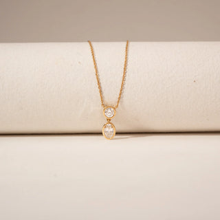 Close-up view of a two-stone diamond pendant in 14KT Yellow Gold, featuring round and oval bezel-set diamonds.