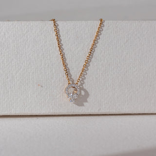 Front view of diamond pendant necklace in yellow gold, featuring a circular halo of round lab-grown diamonds with a floral cluster drop. Set against a textured neutral backdrop, it reflects delicate elegance and shine.