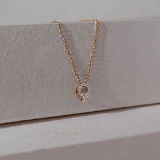 Angled view of diamond pendant necklace in yellow gold, featuring a circular halo of round lab-grown diamonds with a floral cluster drop. Set on a textured neutral surface, it reflects soft sparkle and elegance.