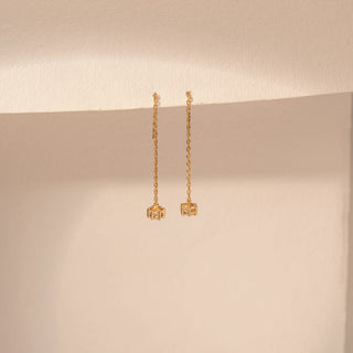Angled view of a 14KT yellow gold earrings featuring round-cut diamonds with delicate chain drops, set against a beige background.