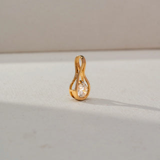 Side view of a yellow gold pendant featuring a bezel-set oval diamond within an infinity-inspired loop design, displayed on a neutral surface with soft natural lighting.