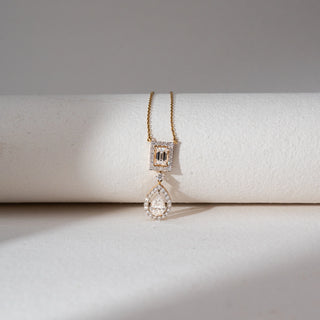 Top view of Dual Drop Diamond Pendant Necklace in 14KT Yellow Gold, featuring an emerald-cut halo with a teardrop lab grown diamond drop below. Placed on a beige backdrop, the design highlights layered brilliance and elegance.
