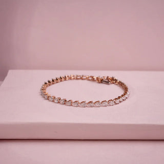 Angled product display of a Réia lab grown diamonds bracelet in rose gold, featuring a continuous row of pear-shaped, placed on a soft blush platform.