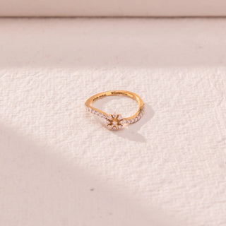 Top view of floral curve diamond ring in yellow gold, featuring a central flower cluster with round lab-grown diamonds and a split pavé band. Placed on a textured beige surface, the design casts a soft shadow.
