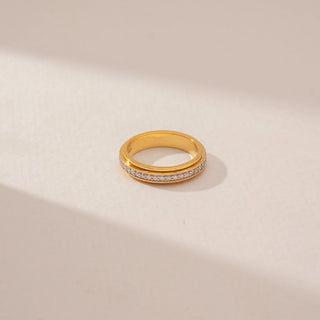 Top view of a diamond band ring in 14KT Yellow Gold, featuring a row of round diamonds between polished gold borders against a beige backdrop.