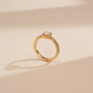Side view of Reia’s 14 KT Yellow Gold Sparkling Solitaire Gold Diamond Ring. It highlights the elevated central round-cut diamond and the shimmering pavé-set band on a cream backdrop.