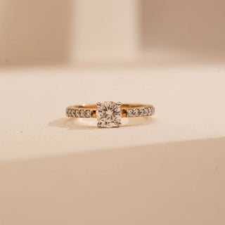 Front view of Reia’s 14 KT Yellow Gold Sparkling Solitaire Gold Diamond Ring. It highlights a central round-cut diamond and a shimmering pavé-set band on a cream backdrop.