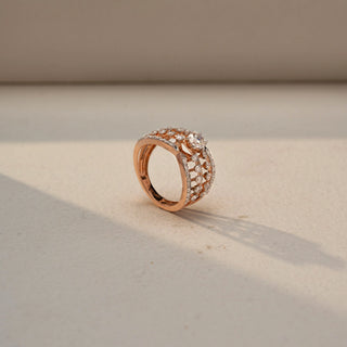 Angled view of a diamond statement ring in 14 KT Rose Gold, featuring an elevated lattice design with pavé-set lab-grown diamonds and a floral-inspired diamond cluster centerpiece, displayed against a beige backdrop.