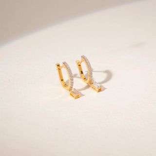 Angled view of 14KT Yellow Gold drop earrings featuring emerald-cut diamonds, pavé-set bars and delicate dangling accents.