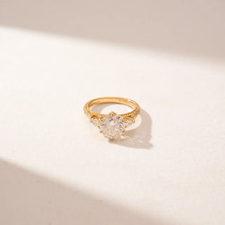 Close-up view of a round diamond ring in 14KT Yellow Gold, featuring a pavé band with intricate detailing against a beige backdrop.