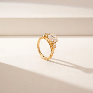 Angled view of a round diamond ring in 14KT Yellow Gold, featuring a pavé band with intricate detailing against a beige backdrop.