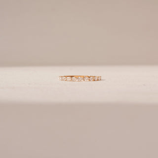 Front view of diamond band ring in 14KT Yellow Gold, featuring a row of diamonds. Captured against a beige backdrop.