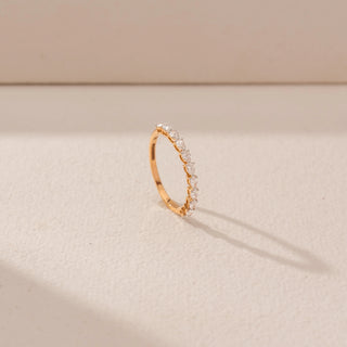 Angled view of diamond band ring in 14KT Yellow Gold, featuring a row of diamonds. Captured against a beige backdrop.