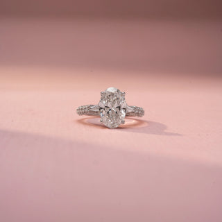 Front view of an oval three-stone engagement ring in White Gold, featuring an oval-cut lab-grown diamond flanked by tapered baguette side diamonds and a pavé-set band, displayed against a soft pink backdrop