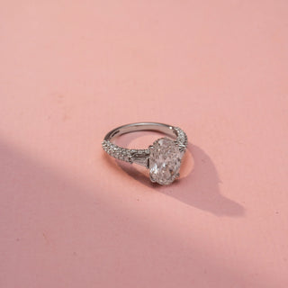 Side view of an oval three-stone engagement ring in White Gold, featuring an oval-cut lab-grown diamond flanked by tapered baguette side diamonds and a pavé-set band, displayed against a soft pink backdrop