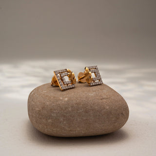 Side view of geometric diamond stud earrings in 14 KT Yellow Gold, featuring pavé-set rectangular frames accented with textured leaf motifs, displayed on a textured stone surface.