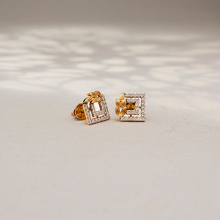 Angled view of geometric diamond stud earrings in 14 KT Yellow Gold, featuring pavé-set rectangular frames accented with textured leaf motifs, displayed on a textured stone surface.