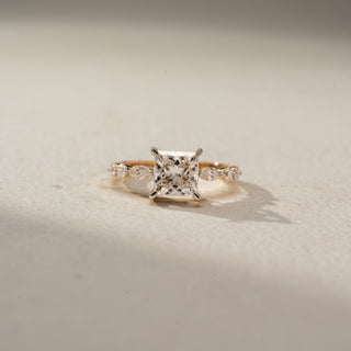 Front view of a princess-cut solitaire engagement ring in 14 KT Yellow Gold, featuring a princess-cut lab-grown diamond accented by marquise-shaped side diamonds along the band, displayed against a beige backdrop.