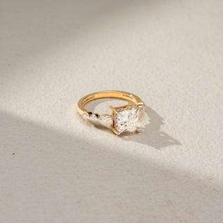 Top view of a princess-cut solitaire engagement ring in 14 KT Yellow Gold, featuring a princess-cut lab-grown diamond accented by marquise-shaped side diamonds along the band, displayed against a beige backdrop.