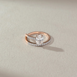Top view of solitaire diamond ring in rose gold, featuring a large oval lab-grown diamond set on a curved dual-band with round diamond accents. Set on a soft neutral surface, it reflects modern elegance and brilliance.