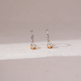 Front view of diamond drop stud earrings in yellow gold, featuring vertical rows of round lab-grown diamonds with a round diamond drop at the base. Set on a soft neutral backdrop, they reflect subtle sparkle.