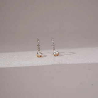 Side angled view of diamond drop stud earrings in yellow gold, featuring vertical rows of round lab-grown diamonds with a pear-shaped diamond drop at the base. Set on a soft neutral backdrop, they reflect elegant sparkle.
