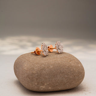 Side view of floral diamond stud earrings in 14 KT Yellow Gold, featuring pavé-set petal motifs radiating from a round center diamond, displayed on a textured stone surface.

