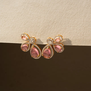 Close up  view of pink gemstone stud earrings in 14 KT Yellow Gold, featuring pear-shaped pink stones accented with halo-set diamonds in a floral-inspired arrangement against a neutral backdrop.
