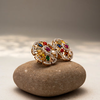 Side view of floral diamond stud earrings in 14 KT Yellow Gold, featuring multicolour gemstones, pearl accents, and pavé-set circular motifs, displayed on a textured stone surface.