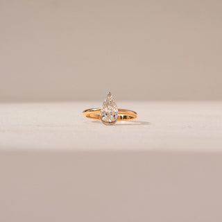 Front view of Pear Diamond Solitaire Ring in 14KT Yellow Gold, featuring a pear-shaped diamond. Captured against a beige backdrop.