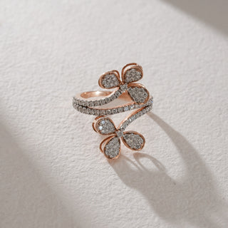 Flat lay of rose gold Twin Flower Diamond Ring crafted in 14 KT hallmarked gold. The two flower-shaped motifs, set with EF colour, VVS clarity diamonds, glisten symmetrically. Pavé-set diamonds extend across the band, creating a luxurious floral aesthetic against a textured neutral background.