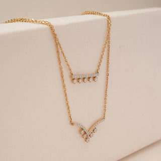 Side view of double layer yellow gold diamond necklace showing pavé diamond bar and curved chevron diamond drop with delicate dangling accents, displayed on a neutral jewellery stand.