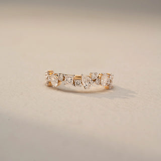 Front view of a Multi-Shape Diamond Eternity Band in 14KT Yellow Gold, featuring mixed oval, pear, and round lab-grown diamonds in a scattered cluster design. Captured against a beige backdrop.